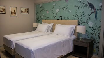 A double bed with white linens, two bedside tables with lamps, and a floral mural on the wall.
