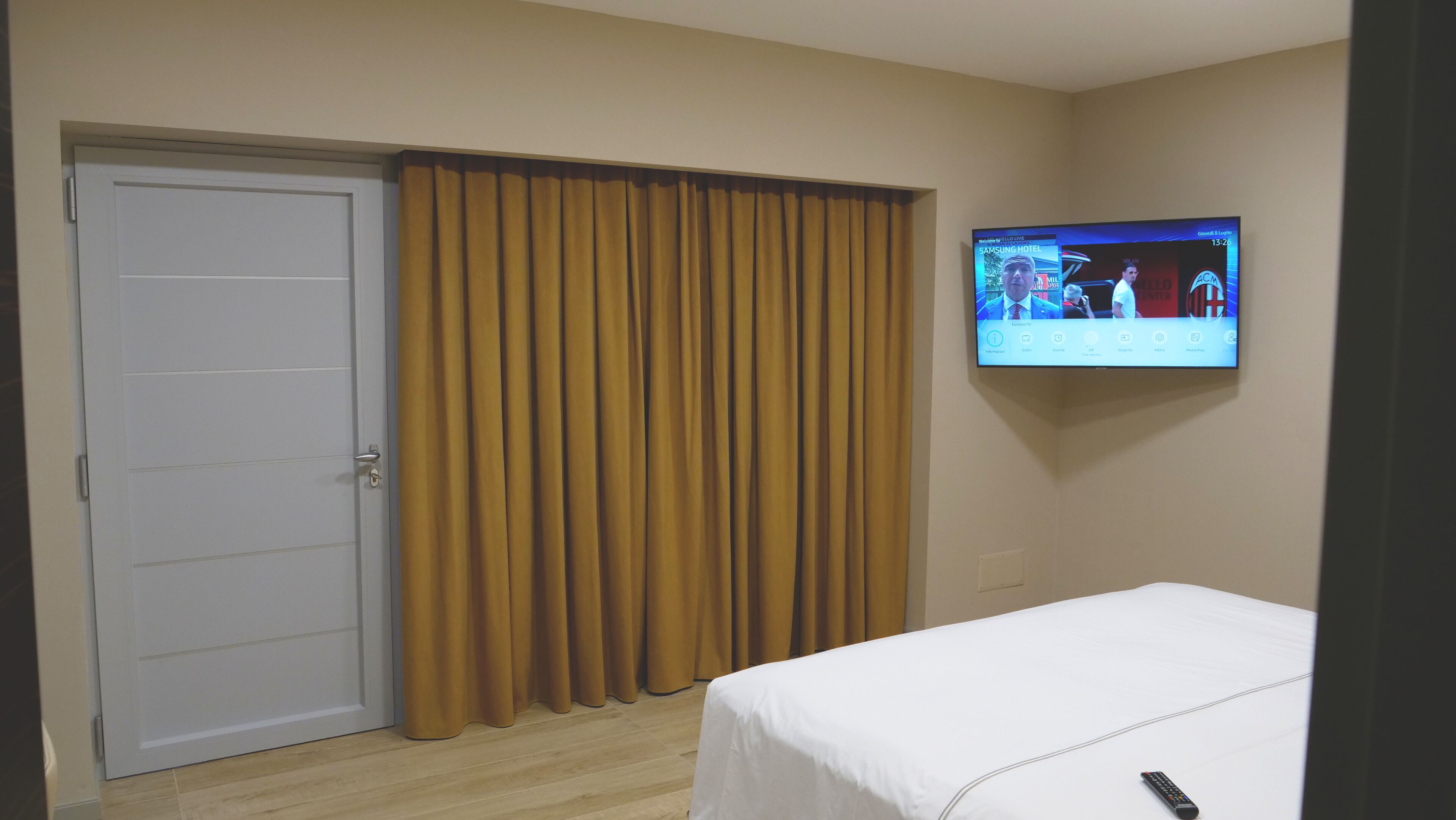 A hotel room with a bed, a television mounted on the wall, a door, and curtains.