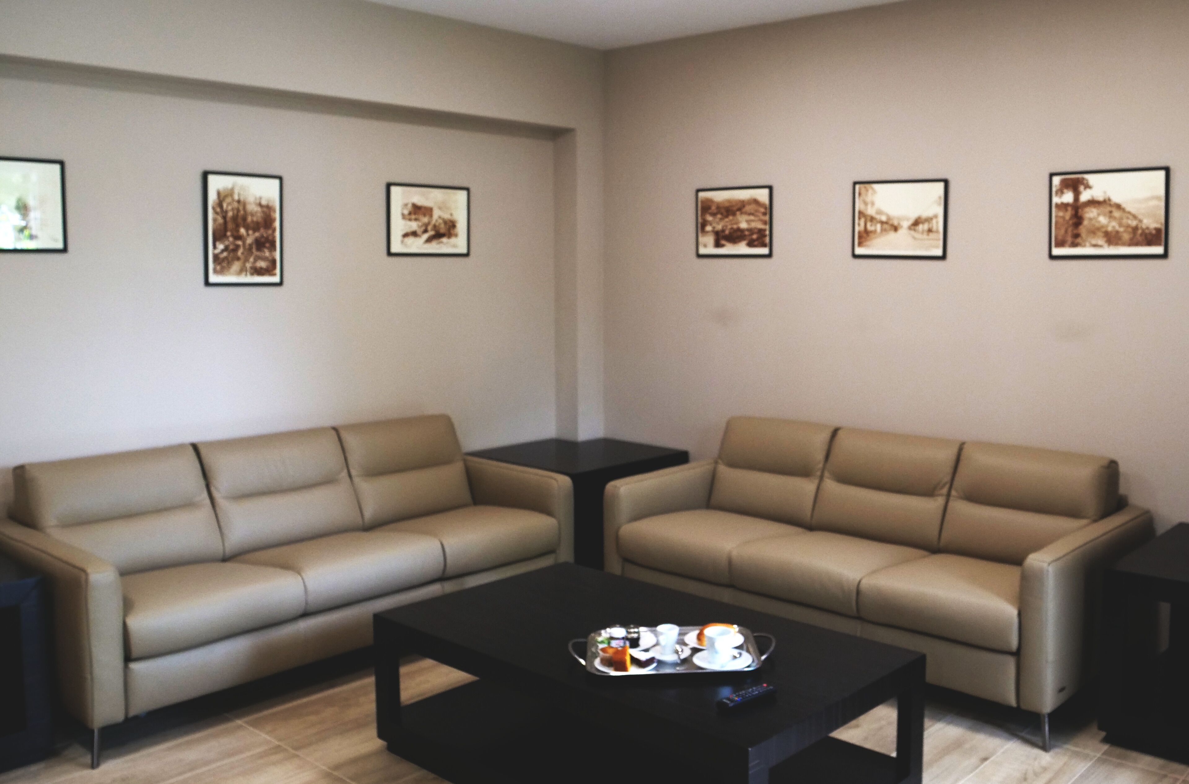 A modern living room with two beige sofas, a black coffee table with a tray of items, and framed pictures on the walls.