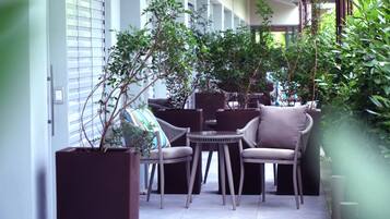 A cozy outdoor seating area with wicker furniture, potted plants, and a view of the building's interior.