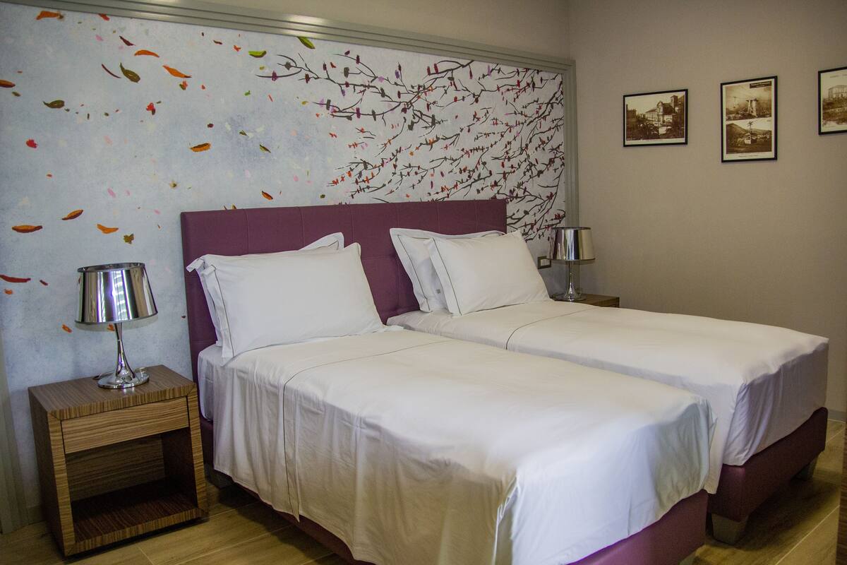 A double bed with white linens, a purple headboard, and two bedside tables with lamps.