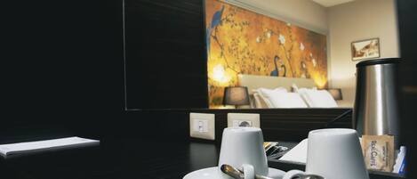 A hotel room with a modern design, featuring a large abstract painting on the wall, a bed with white linens, and a coffee station with two cups and a thermos.