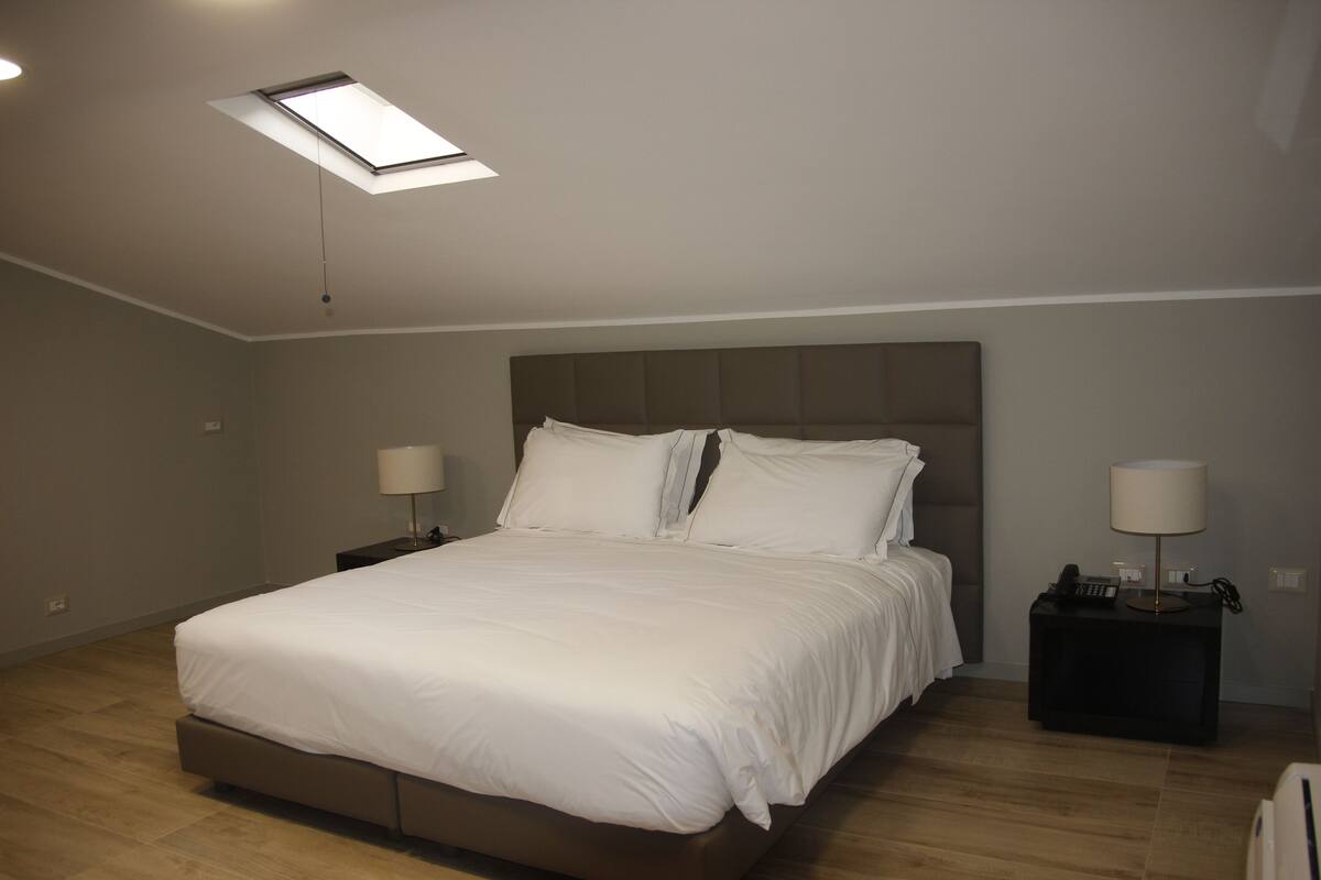 A bedroom with a bed, two bedside tables, a ceiling light, and a skylight.