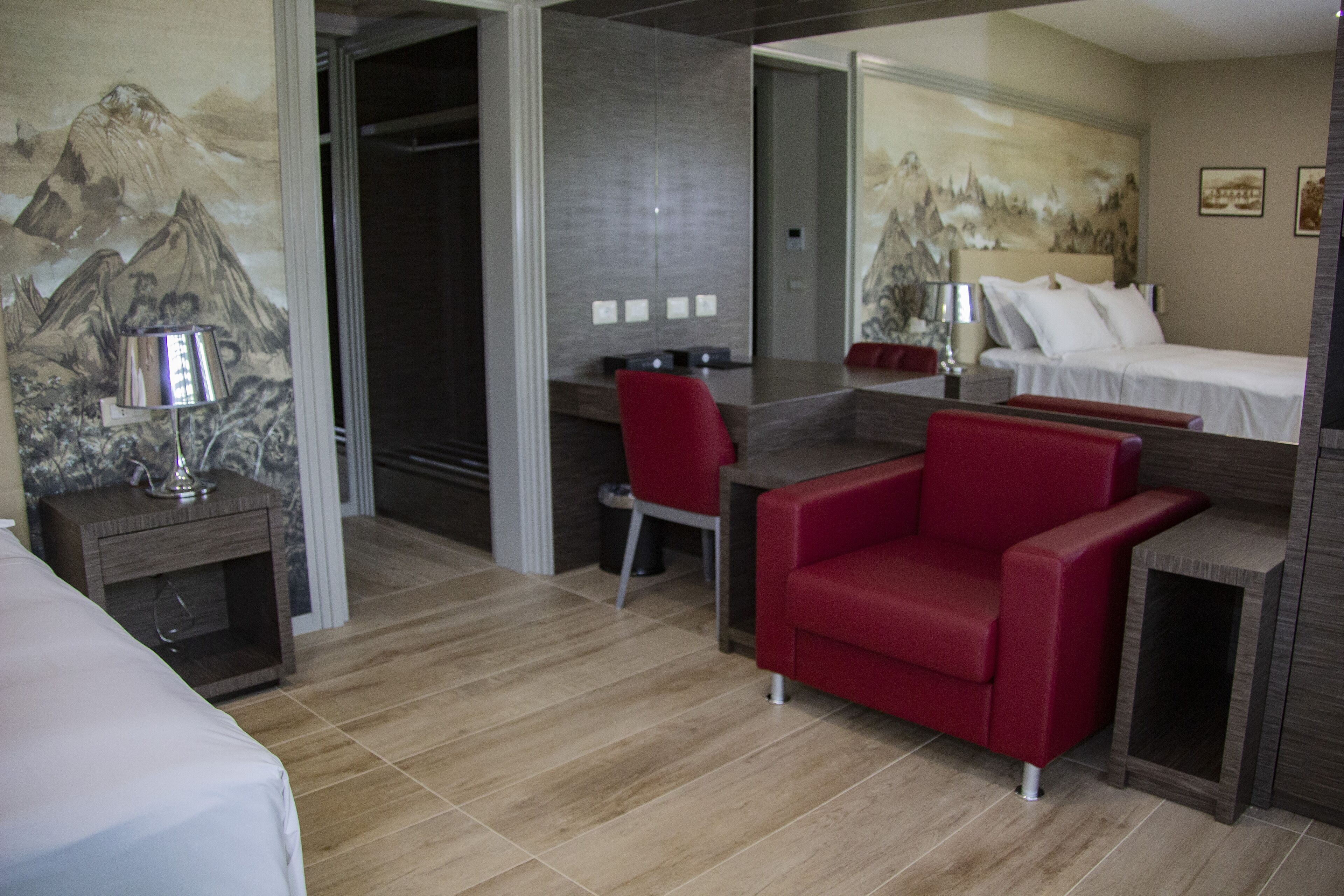 A hotel room with a bed, a desk, a red chair, and a small table.