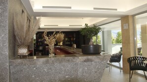 A modern reception area with a marble counter, decorative plants, and a view of the outdoor seating area. - Kairos Resort (Piedimonte San Germano)