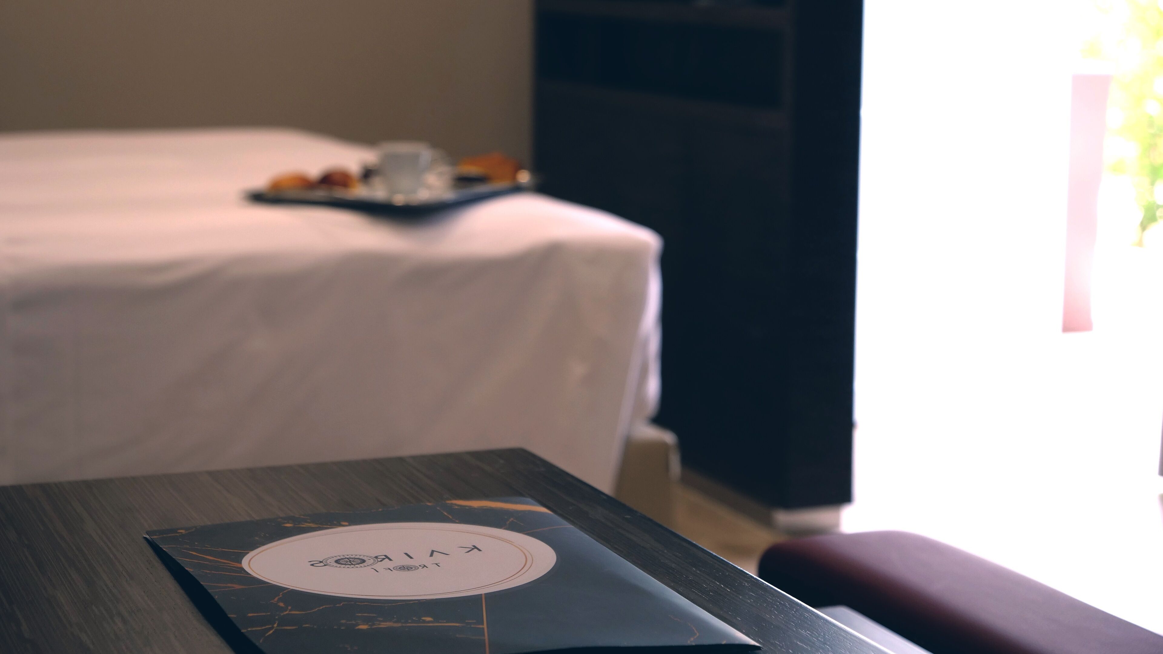 A hotel room with a neatly made bed, a tray of snacks on the bed, and a table with a menu or information card.
