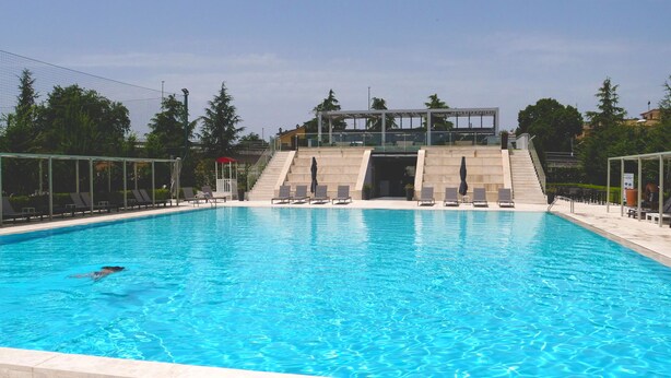 A swimming pool with a person swimming, surrounded by a fence, and a covered area with steps leading up to a building. - Kairos Resort (Piedimonte San Germano)