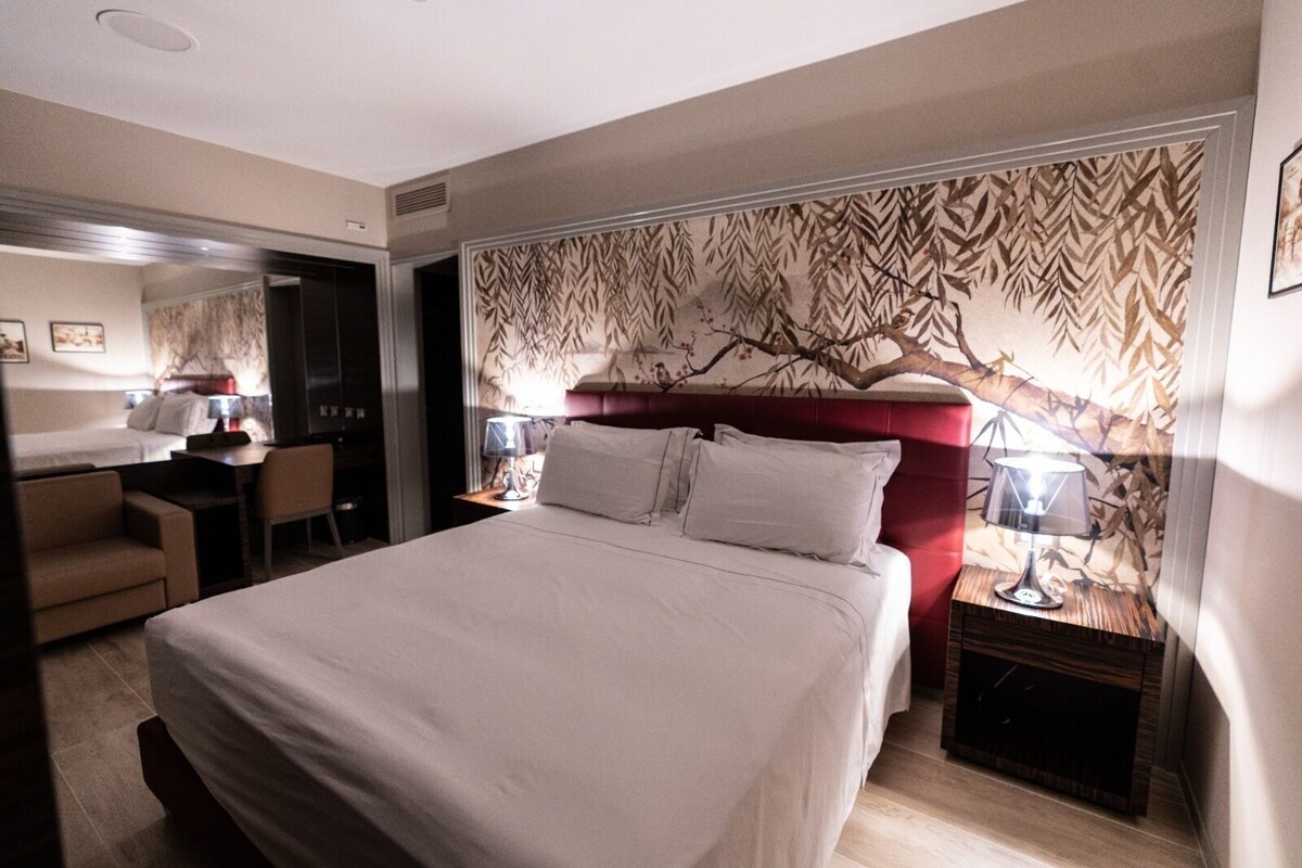 Una habitación de hotel con una cama grande, un escritorio, una silla y una mesita de noche con lámparas.