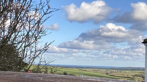 A view from a terrace with a brick floor, overlooking a rural landscape with fields and a distant bridge. - Contemporary Guest House With Outside Barrel Sauna (Wadebridge)