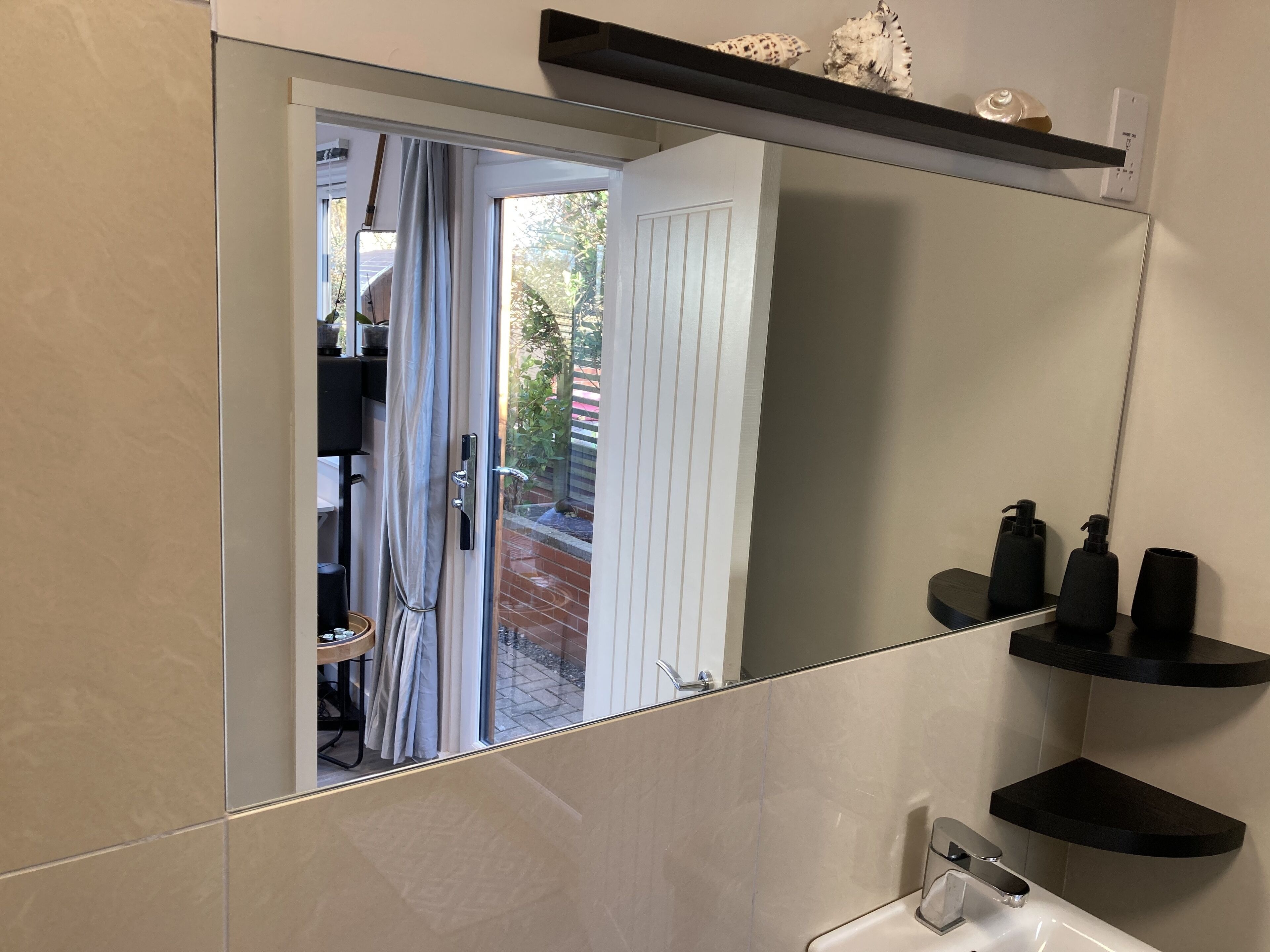 A bathroom with a large mirror, a sink, and black shelves.