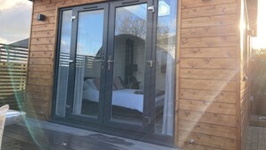A wooden cabin with a glass door leading to a bedroom with a bed and a window. - Contemporary Guest House With Outside Barrel Sauna (Wadebridge)