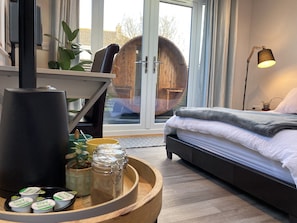 A modern bedroom with a bed, bedside table, and a large window. - Contemporary Guest House With Outside Barrel Sauna (Wadebridge)