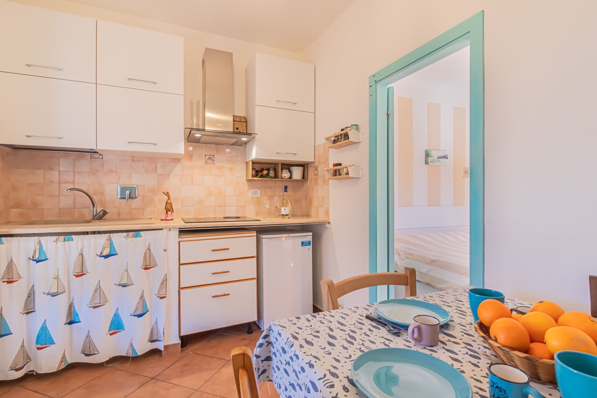 A compact kitchen with white cabinets, a stainless steel range hood, and a small refrigerator.