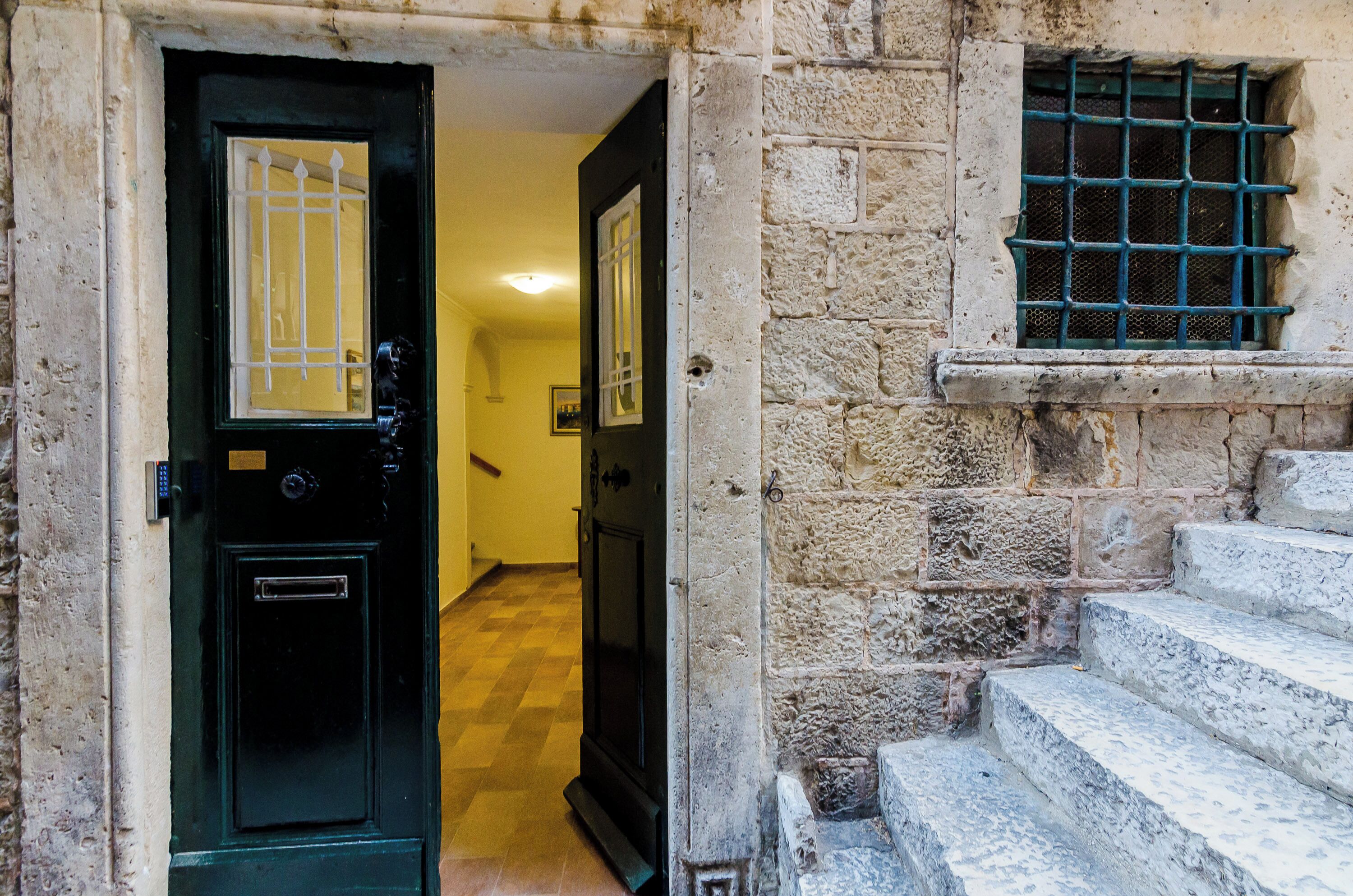 A doorway with a black door and a window with metal bars, leading to a staircase.