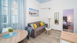 Ein modernes Wohnzimmer mit einer grauen Couch, einem runden Holztisch mit blauer Tischmatte und einem kleinen weißen Beistelltisch.