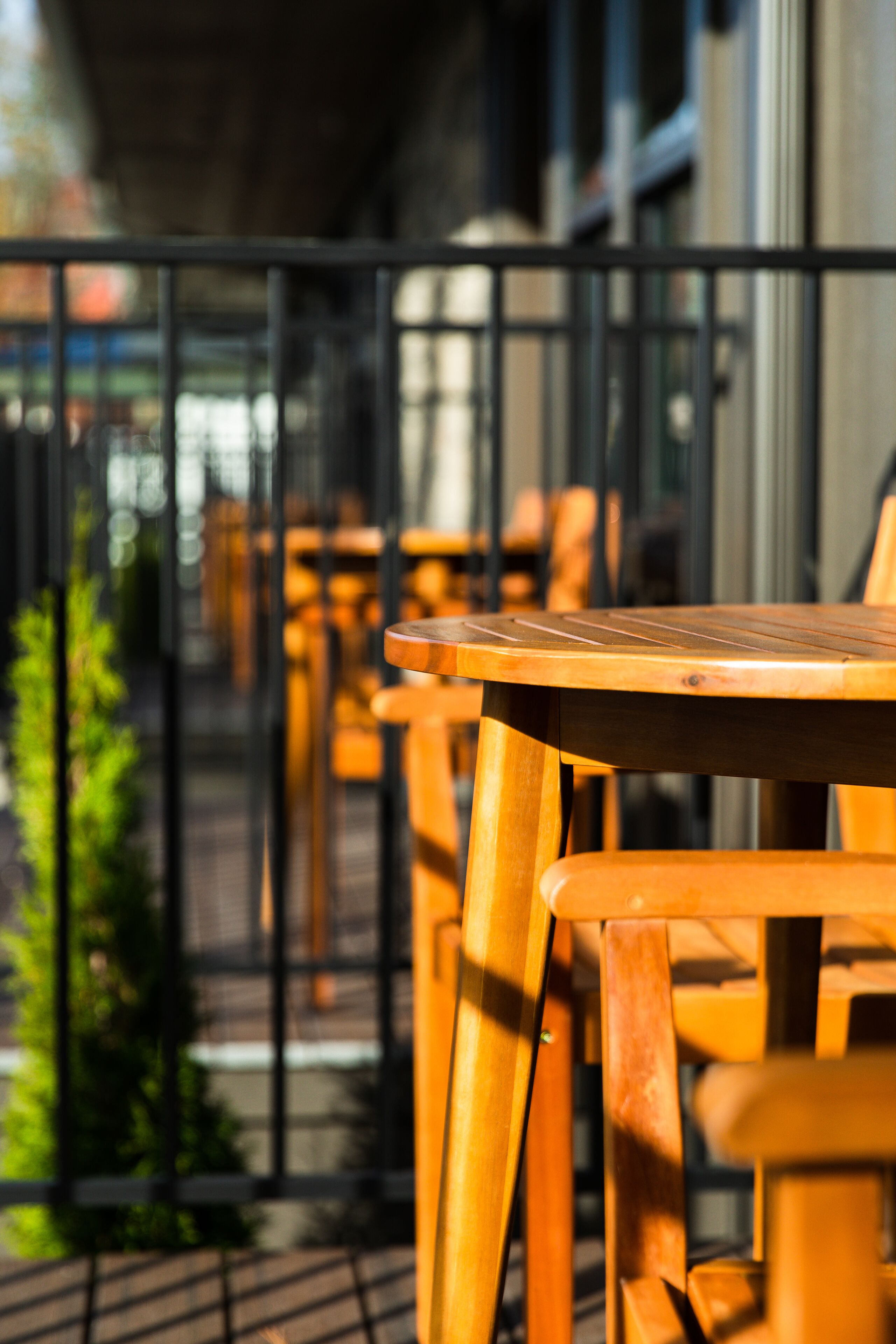 A row of wooden tables and chairs on an outdoor balcony with a metal railing.