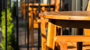 A row of wooden tables and chairs on an outdoor balcony with a metal railing.