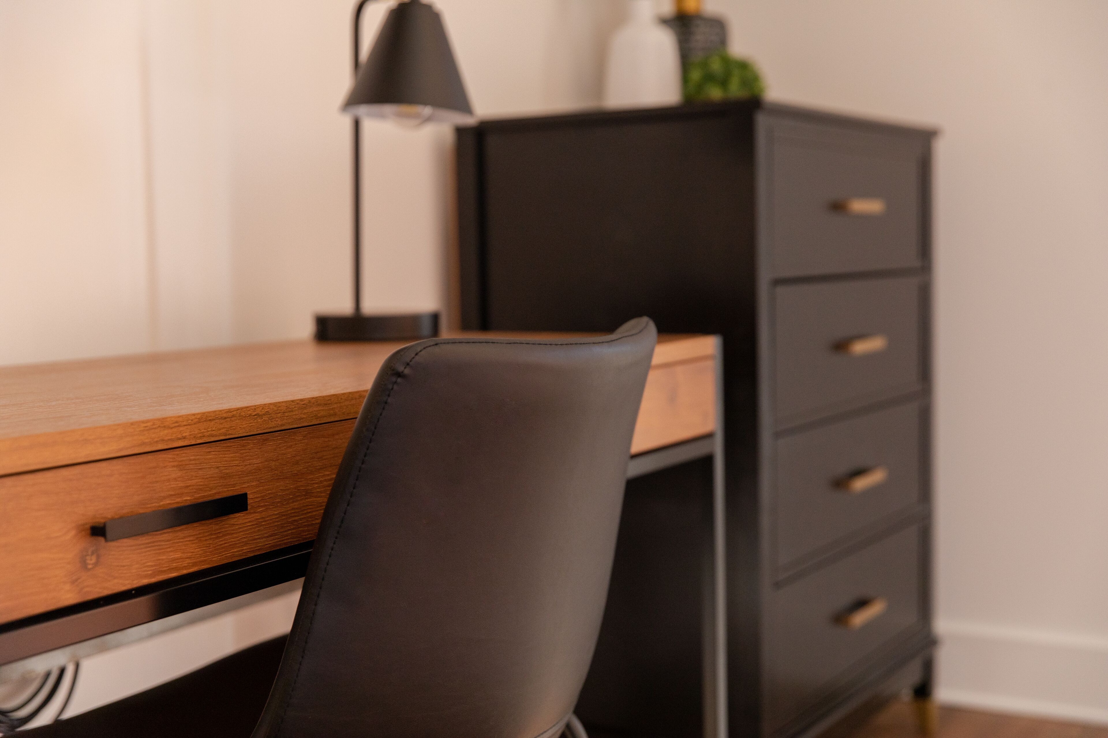 Un escritorio moderno con una silla de cuero, una lámpara y un archivador.