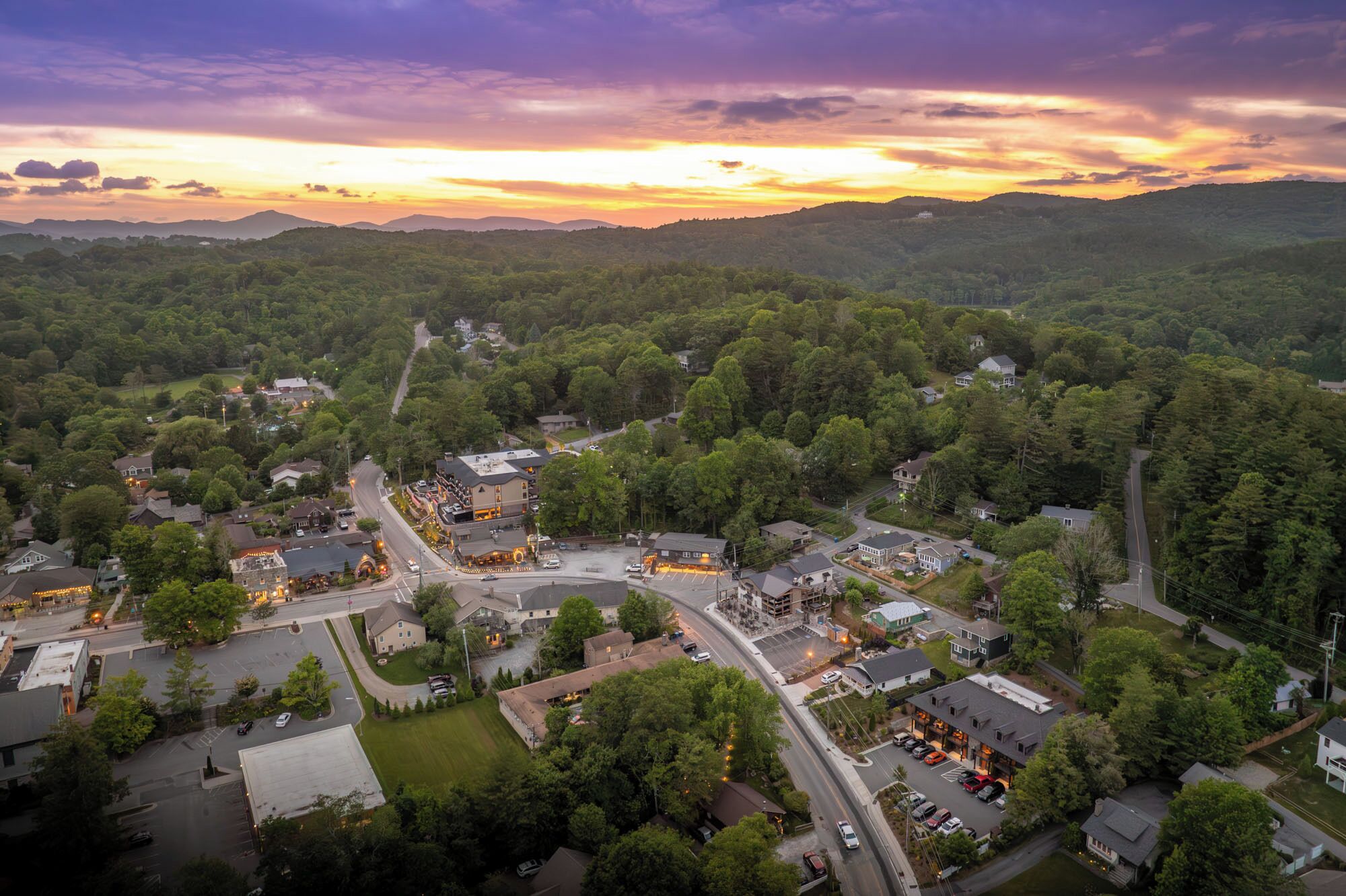 An aerial view of a town with a mix of residential and commercial buildings, surrounded by dense forests and hills.