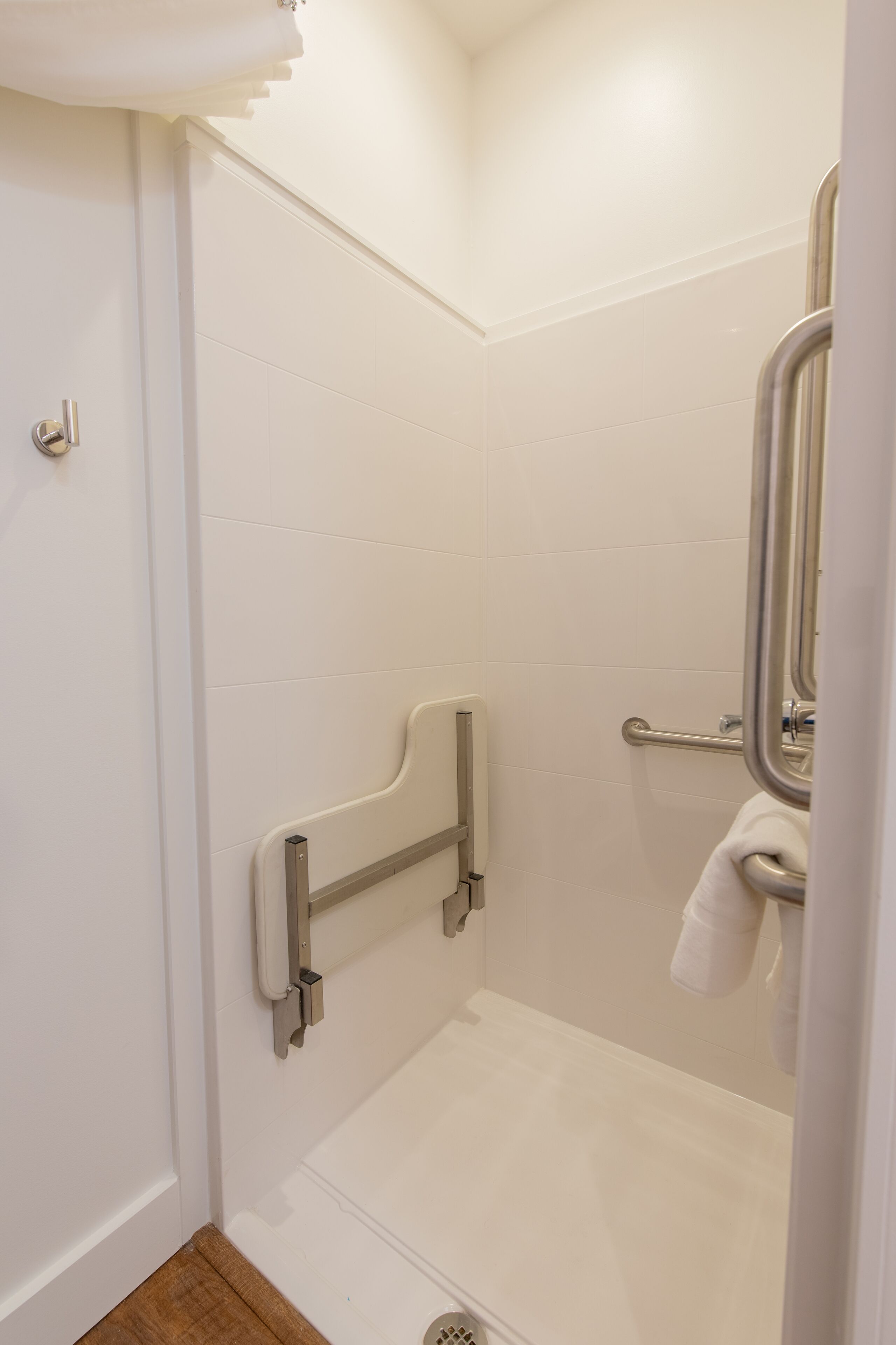 A bathroom with white tiled walls, a shower area, a grab bar, and a towel hanging on a rack.