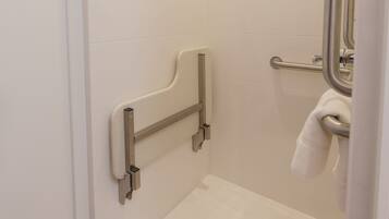 A bathroom with white tiled walls, a shower area, a grab bar, and a towel hanging on a rack.
