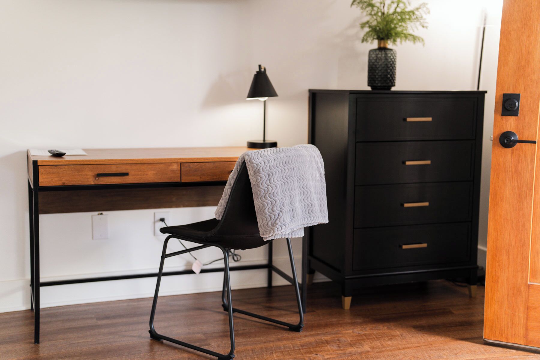 Et arbejdsområde med et træskrivebord, en sort stol, en sort lampe og et sort arkivskab.
