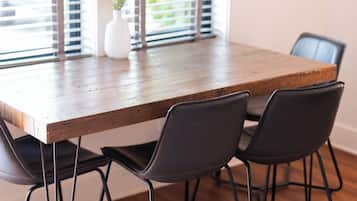 A dining table with four chairs, a vase with flowers, and a window with blinds.