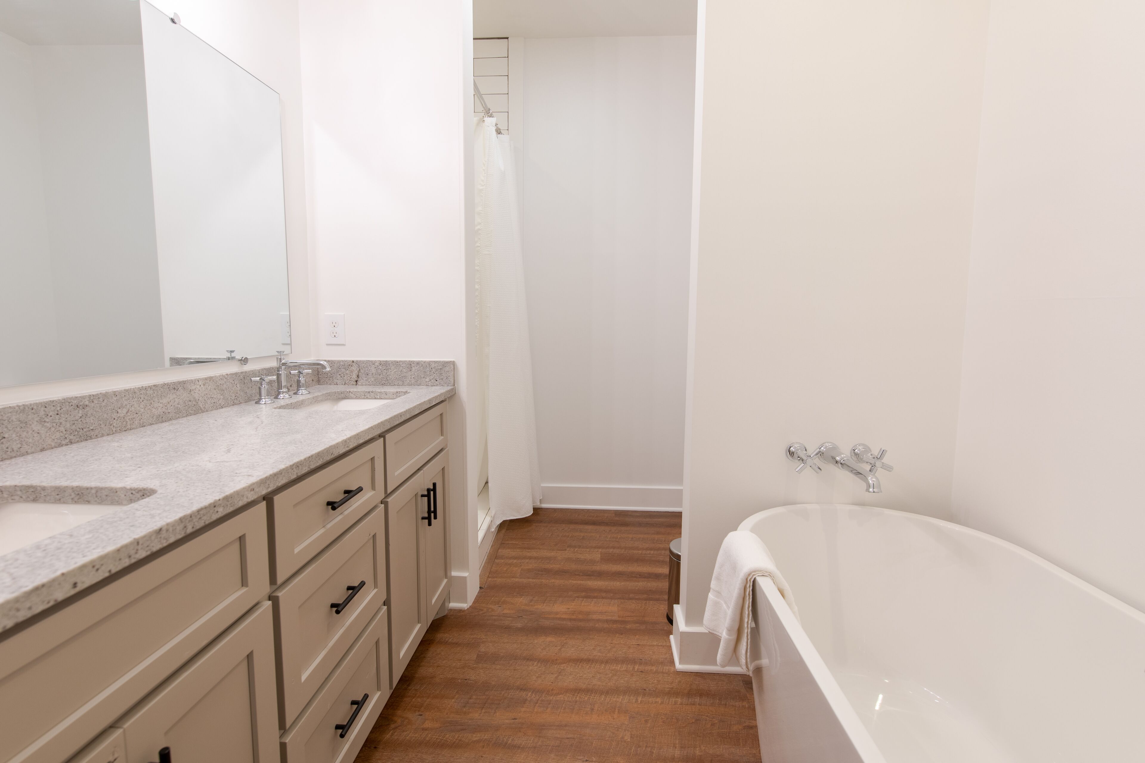 Un bagno con doppio lavabo, vasca e pavimento in legno.