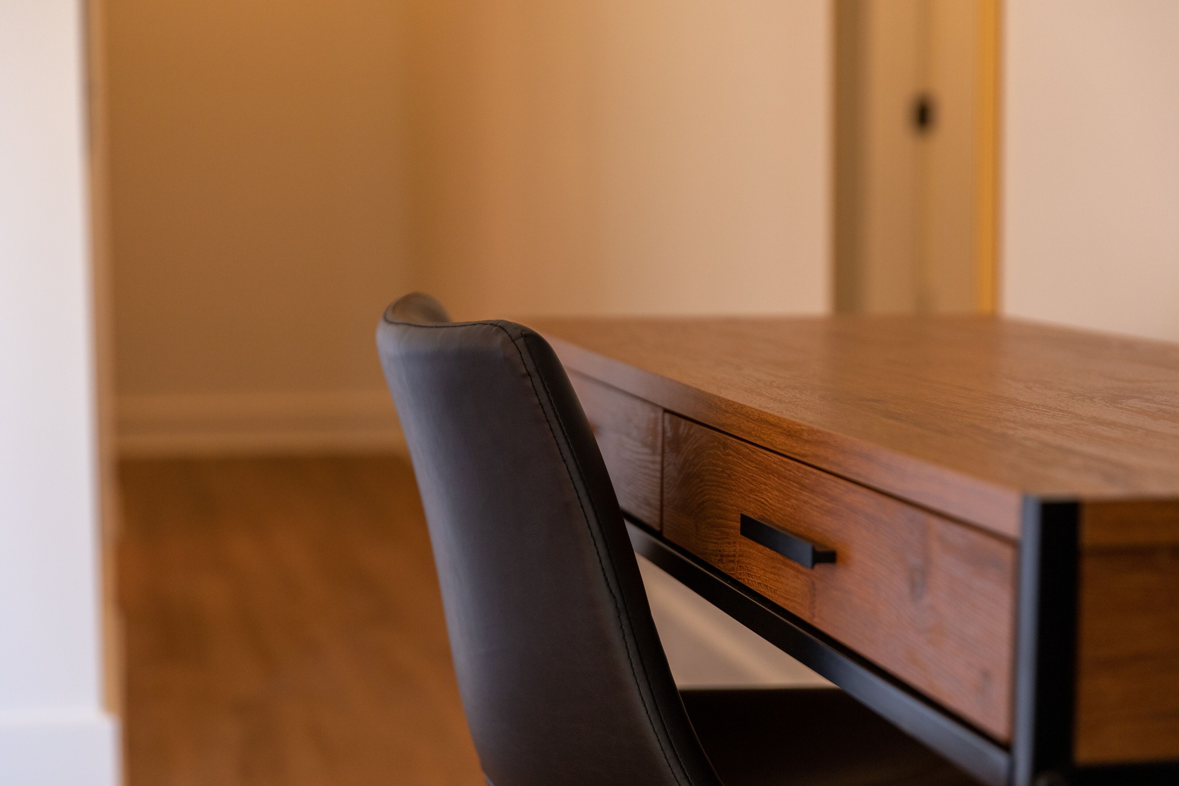 A wooden table with a drawer and a black chair.