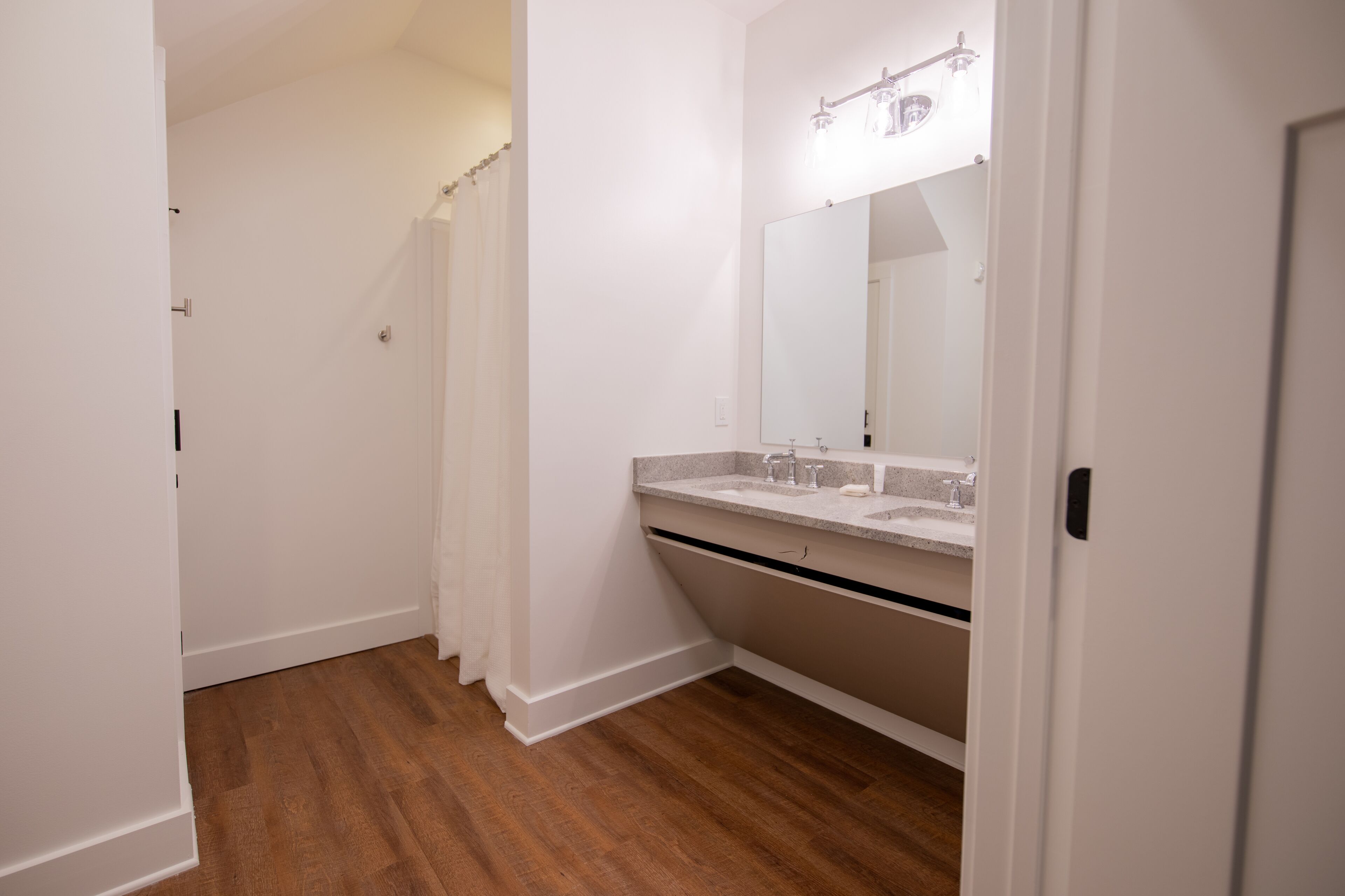 Une salle de bain avec un plancher en bois, un lavabo blanc et un miroir au-dessus.