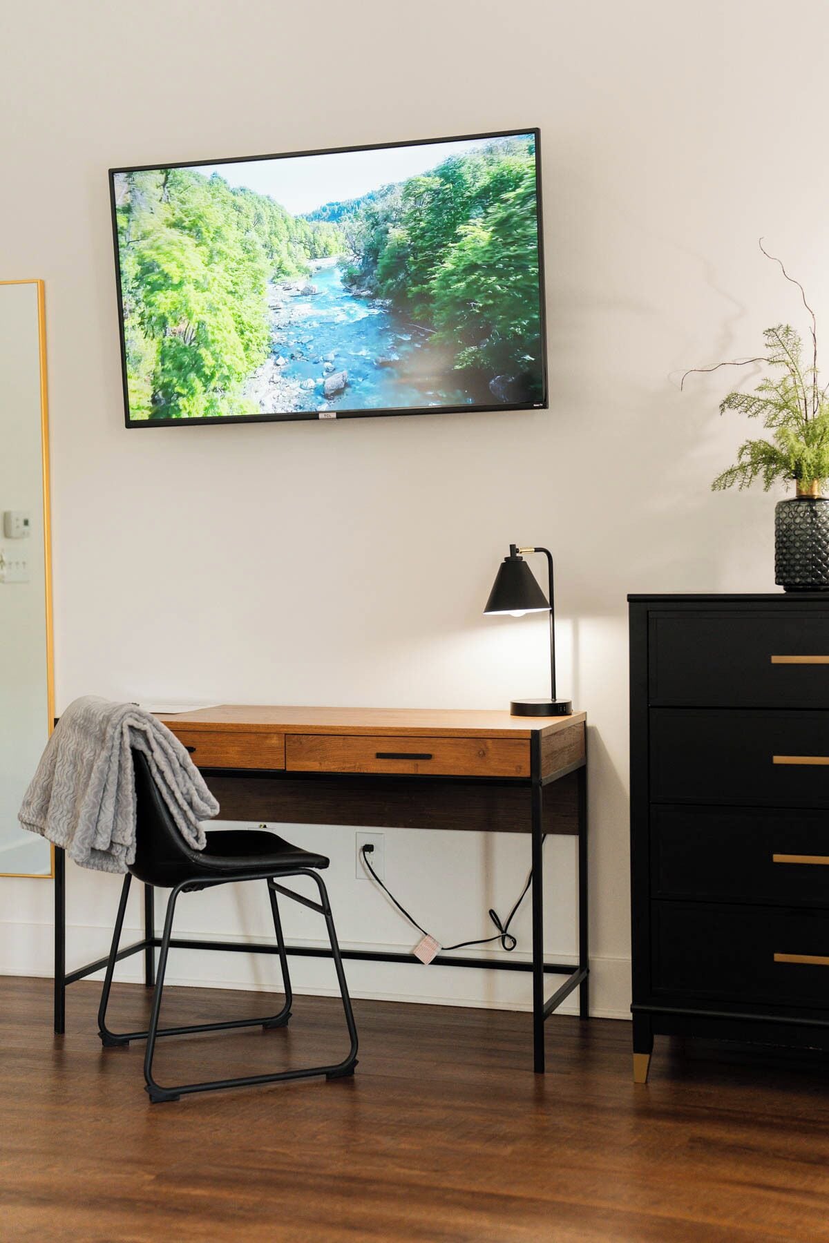 Un espace de travail moderne avec un bureau en bois, une chaise noire, une lampe noire et une commode noire dotée de tiroirs.