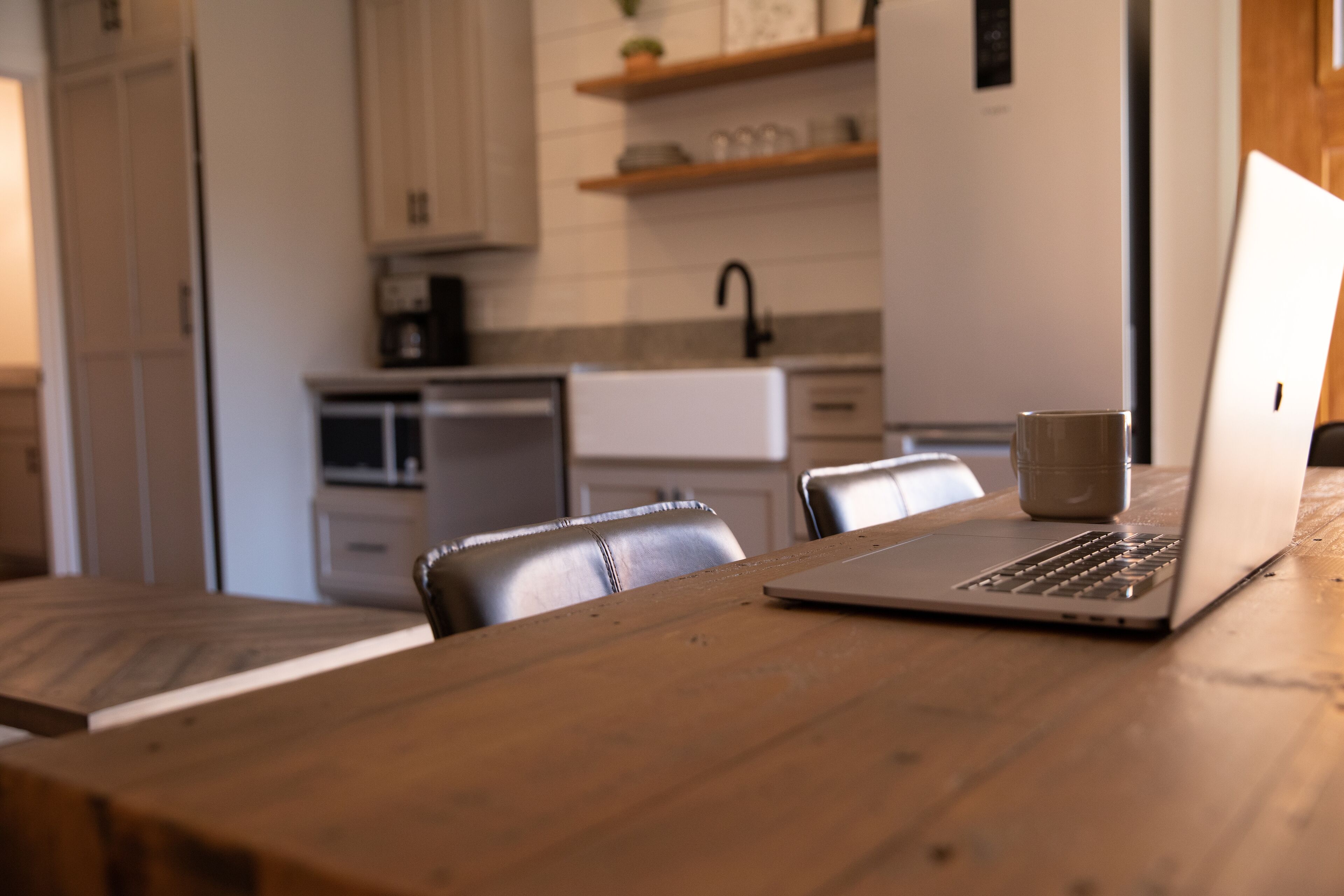 A wooden dining table with a laptop and a mug.