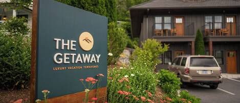 A sign for 'The Getaway' luxury vacation townhomes with a view of a building and a car parked nearby.