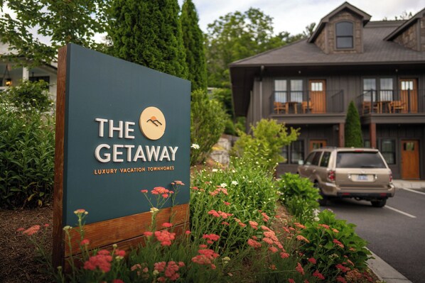 A sign for 'The Getaway' luxury vacation townhomes with a view of a building and a car parked nearby.
