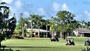 Un campo da golf con uno stagno, palme e un club house sullo sfondo.