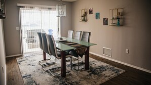 Zona pranzo con tavolo in vetro, sedie in pelle, tappeto decorato e vista attraverso una finestra con persiane.