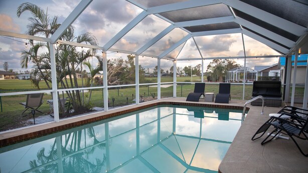Una piscina interna con soffitto in vetro, circondata da poltrone relax e palme.