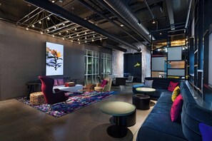 A modern lounge area with seating, a large abstract painting, and exposed ductwork on the ceiling. - Aloft by Marriott Austin Southwest (Austin)