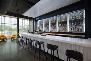 A bar area with a long counter, multiple stools, and a large window. - Aloft by Marriott Austin Southwest (Austin)