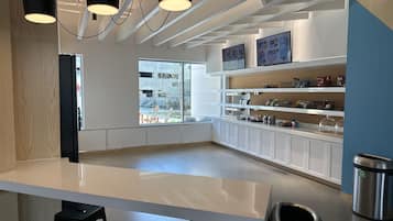 A modern cafe with a clean, minimalist design, featuring a white counter, black stools, and a large window offering a view of the outside.