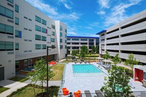 A modern building with a swimming pool, outdoor seating, and a parking garage. - Aloft by Marriott Austin Southwest (Austin)