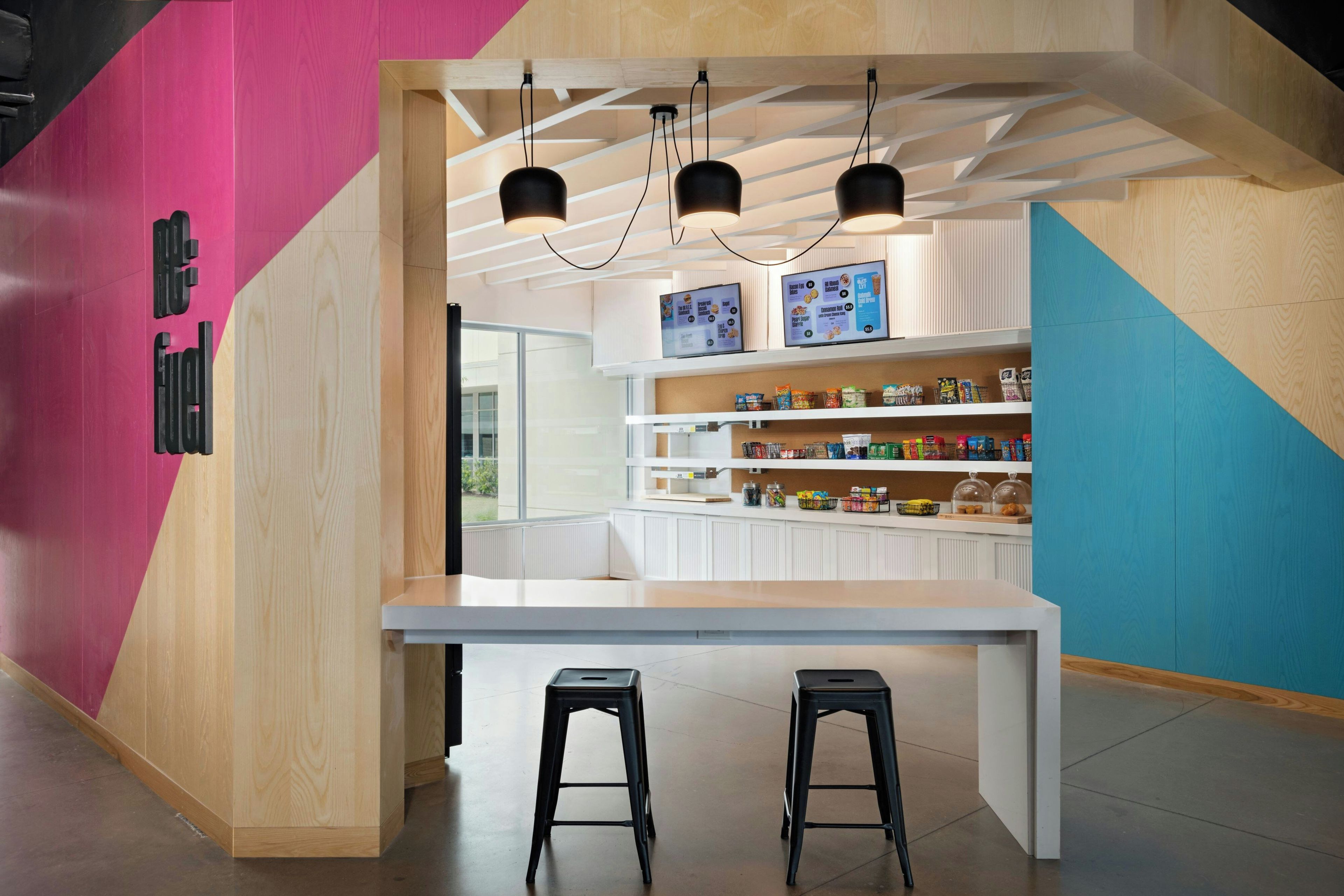 A modern cafe with a white counter, black stools, and a colorful interior design.