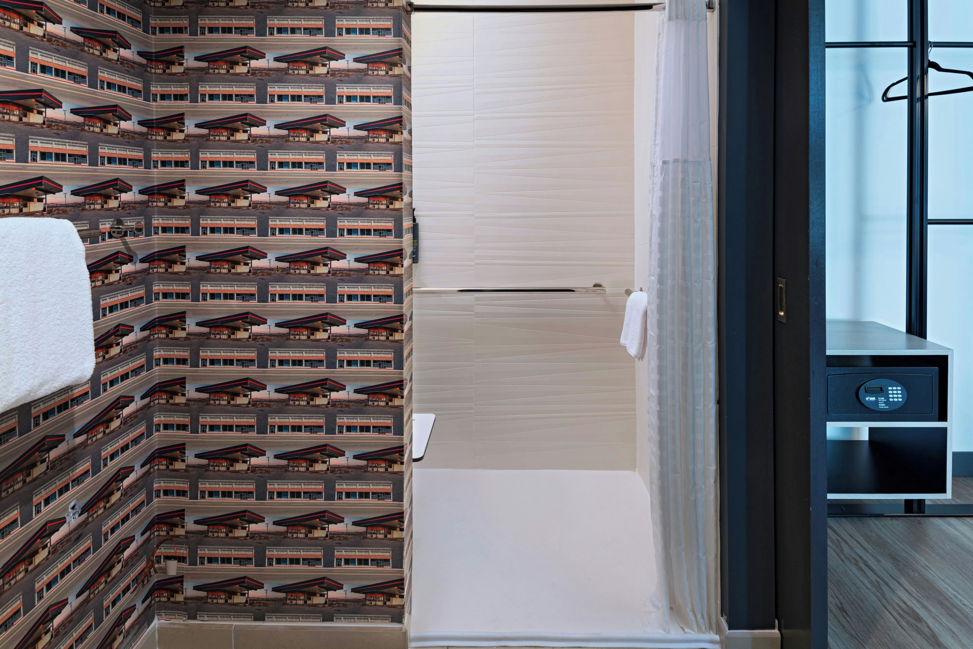 Habitación de hotel con papel tapiz estampado, una puerta de madera, una toalla blanca y un pequeño panel de control.