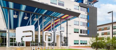 Un moderno edificio de hotel con un gran letrero 'aloft hotels', un acceso cubierto y un césped bien cuidado.