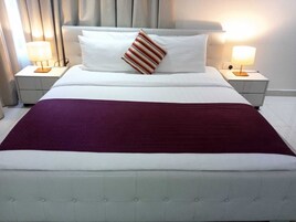 Una habitación de hotel con una cama grande, dos mesitas de noche y un cabecero.