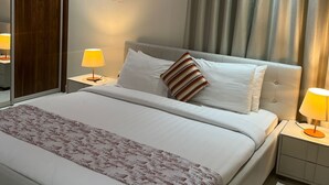 Een keurig opgemaakt slaapkamer met een groot bed, twee nachtkastjes met lampen, een kledingkast en een raam met gordijnen.