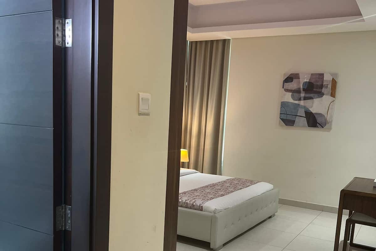 A hotel room with a bed, a small table, a painting on the wall, and a ceiling light.