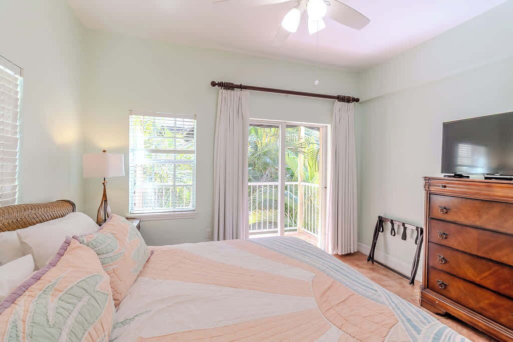 A bedroom with a bed, a dresser, a television, a window with curtains, and a ceiling fan.