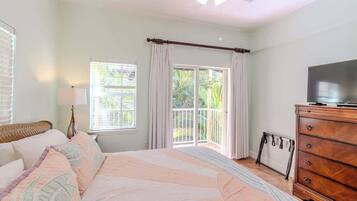 A bedroom with a bed, a dresser, a television, a window with curtains, and a ceiling fan.