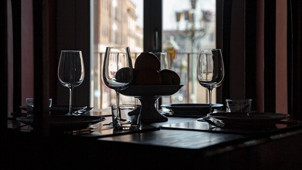 Una mesa de comedor con copas de vino y un frutero, frente a una ventana con vistas a la ciudad.